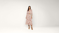 A woman stands against a plain background wearing a light pink floral jacket and matching wide-leg skirt with tan heels.