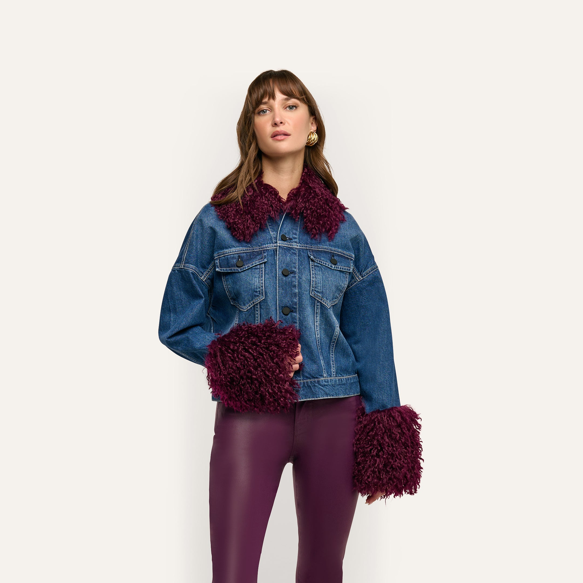 A woman wears a cropped blue Bronson Jean Jacket with deep purple faux fur trim on the collar and cuffs over purple leggings.