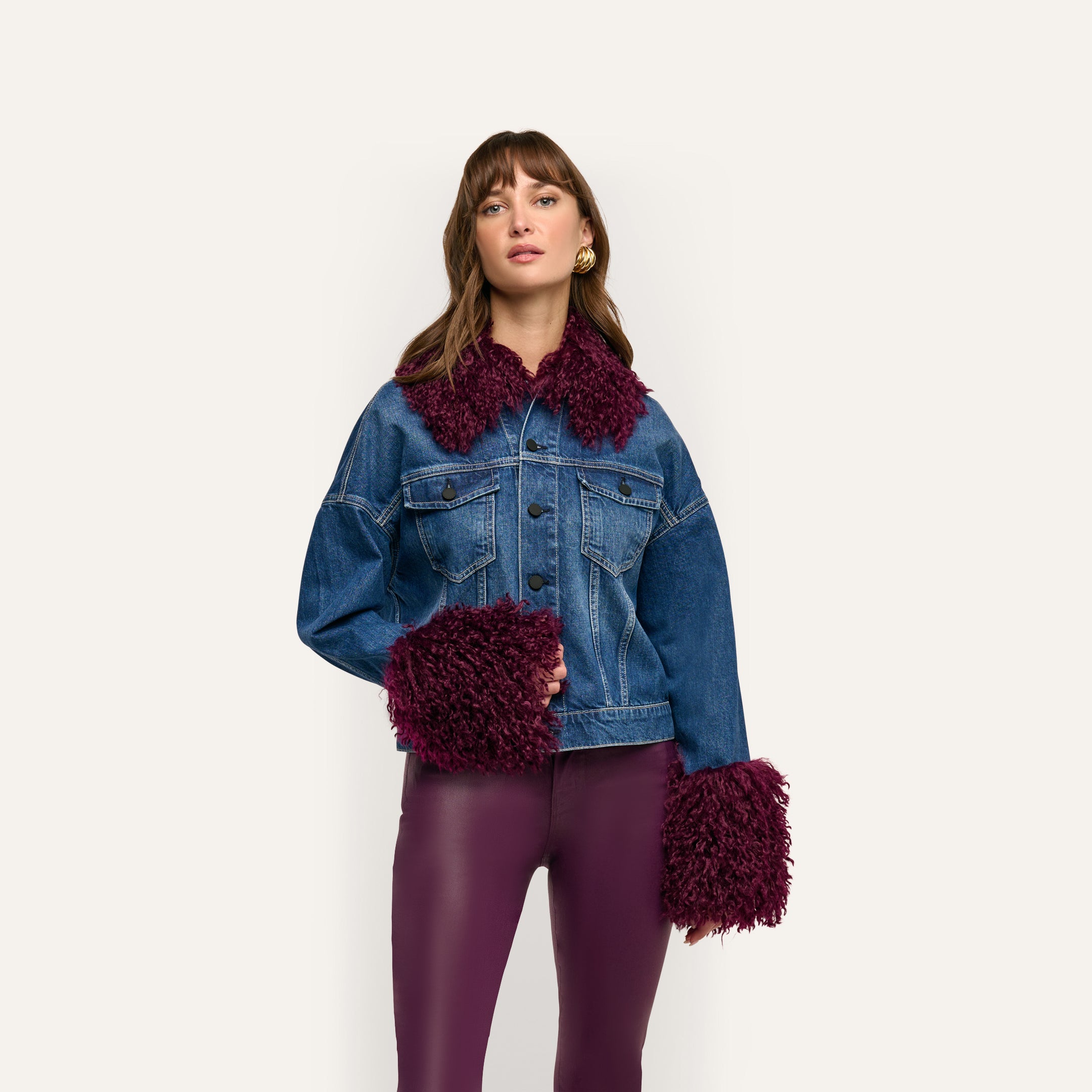 A woman wears a cropped blue Bronson Jean Jacket with deep purple faux fur trim on the collar and cuffs over purple leggings.