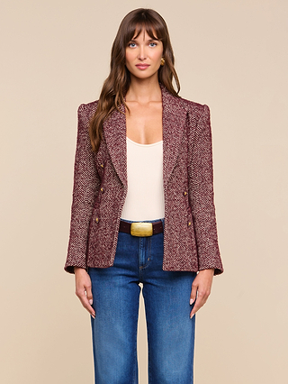 A woman with long brown hair wears the Karima Tweed Blazer over a cream top, blue jeans, and a belt with a gold buckle, standing against a beige background.