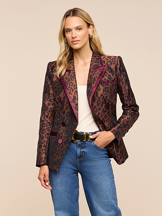 A woman with long blonde hair stands against a neutral background wearing the Kyomi Double-Breasted Blazer in a brown and burgundy leopard jacquard, paired with a beige top, blue jeans, and a black belt.