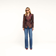 A person wearing sunglasses, the Kyomi Double-Breasted Blazer in leopard jacquard, blue jeans, and brown shoes stands against a plain white background.