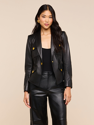 A woman wearing the Wisteria Leather Blazer with gold buttons and matching black leather pants stands against a plain beige background.
