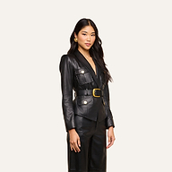 A woman with long dark hair wears the Wisteria Leather Blazer—a fitted black leather jacket with gold buttons—paired with matching pants, standing confidently against a plain light background.