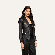 A woman with long, wavy hair wears the fitted Wisteria Leather Blazer with gold buttons and matching black leather pants, standing against a plain light background.