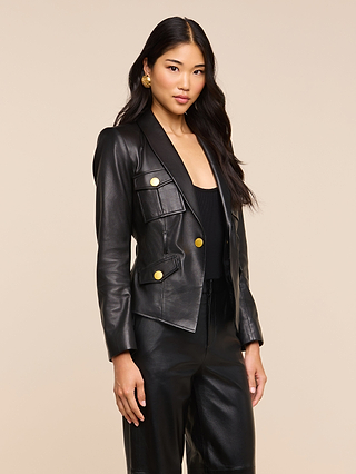 A woman with long black hair wears the Wisteria Leather Blazer, a fitted black jacket with gold buttons and matching leather pants, standing against a plain light background. The blazer’s lightweight leather adds a modern edge to her sophisticated look.