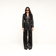 A woman wearing the Wisteria Leather Blazer with gold buttons, wide-leg black leather pants, and sunglasses stands against a plain white background.