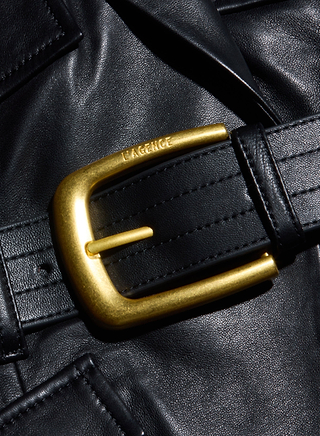 A close-up of a black leather belt with a shiny gold buckle resting on a black leather surface, reminiscent of the refined texture found in the Wisteria Leather Blazer. The word LAFAYETTE is engraved on the buckle.