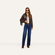 Wearing the Luci Fringed Leather Jacket, a woman in sunglasses, blue jeans, and brown boots stands confidently against a plain light background.