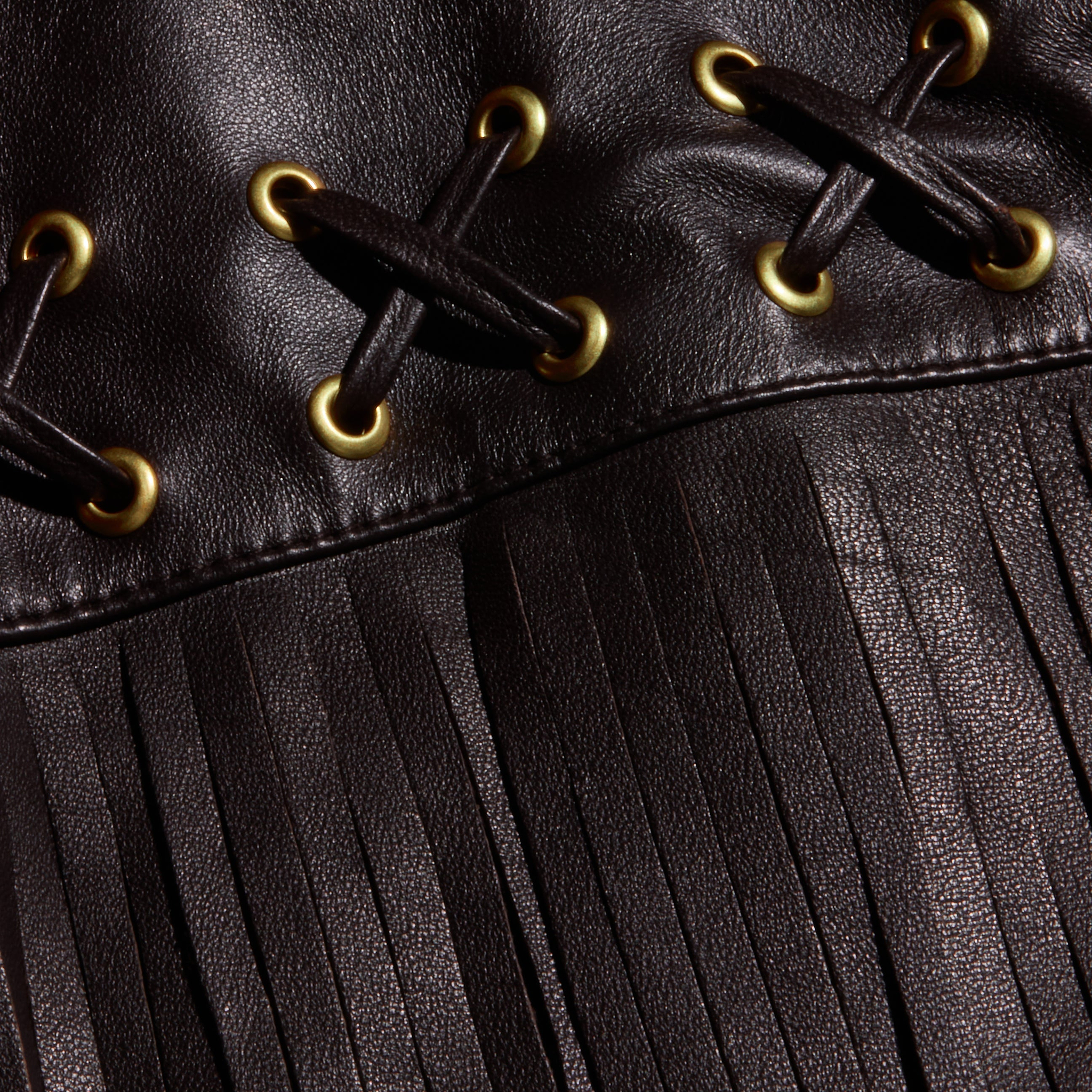 Close-up of the Luci Fringed Leather Jacket, featuring black leather with gold eyelets, black lacing in an X pattern, and a long fringe detail at the bottom.