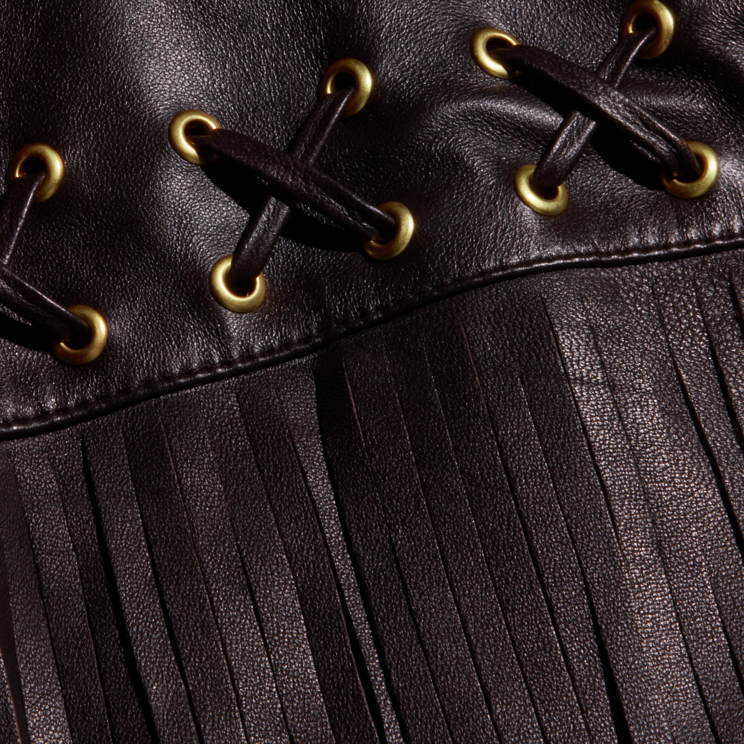Close-up of the Luci Fringed Leather Jacket, featuring black leather with gold eyelets, black lacing in an X pattern, and a long fringe detail at the bottom.