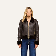 A person wearing the Glacia Shearling Jacket—a dark brown aviator style with fur trim—paired with blue jeans stands facing forward against a plain, light background.