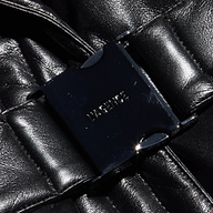 Close-up of the Ignis Puffer Vest, a black, shiny quilted vegan leather vest featuring a rectangular black buckle at the center embossed with LASERICE.