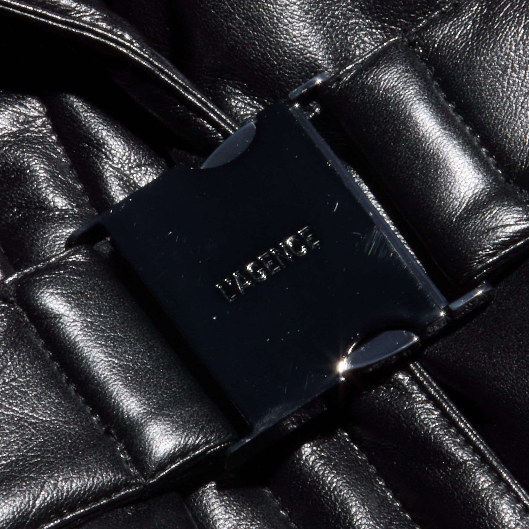 Close-up of the Ignis Puffer Vest, a black, shiny quilted vegan leather vest featuring a rectangular black buckle at the center embossed with LASERICE.