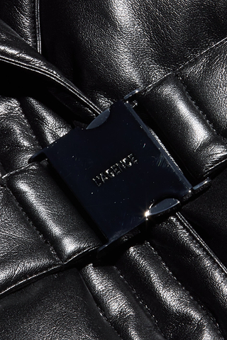 A close-up of the shiny black metal buckle embossed with DIESIRE, fastened on quilted black vegan leather, highlights the texture and sheen of the material—making the Ignis Puffer Vest a sophisticated choice for transitional outerwear.