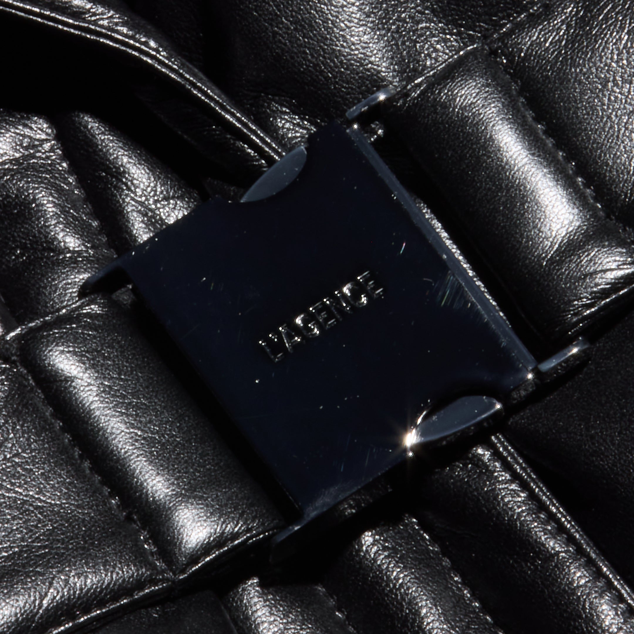 Close-up of the Ignis Puffer Vest, a black, shiny quilted vegan leather vest featuring a rectangular black buckle at the center embossed with LASERICE.