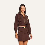 Woman wearing the Kade Windbreaker, a brown cropped jacket with large gold buttons and pockets, paired with a matching high-waisted skirt, gold jewelry, and a black belt.