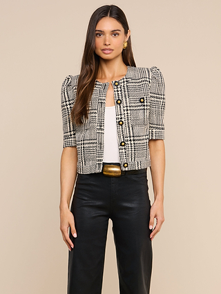 A woman stands against a beige background, looking directly at the camera, wearing the Allegra Cropped Tweed Jacket with gold buttons over a white top and black pants.
