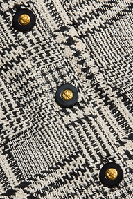 Close-up of black and white patterned fabric from the Allegra Cropped Tweed Jacket, featuring a round black button with a textured gold center. The fabric showcases zigzag and grid designs, creating a woven, textured appearance.