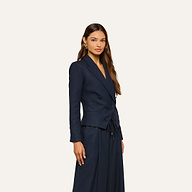 A woman poses against a plain light background, looking forward with a neutral expression, wearing the Risa Double-Breasted Blazer in navy blue with matching wide-leg pinstriped pants.