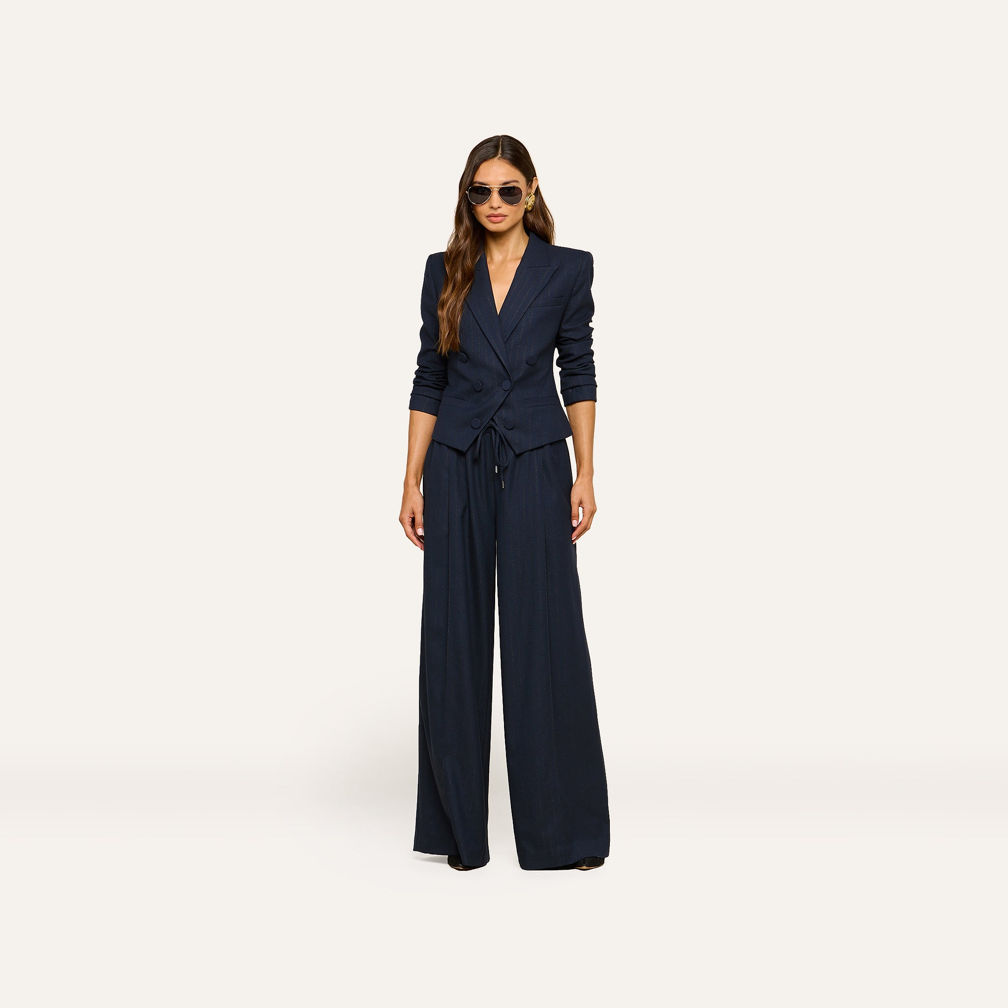 A woman wearing sunglasses and the Risa Double-Breasted Blazer with wide-leg trousers stands facing forward against a plain light background.