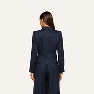 A woman with long brown hair stands facing away, wearing the Risa Double-Breasted Blazer and matching trousers against a plain light background.