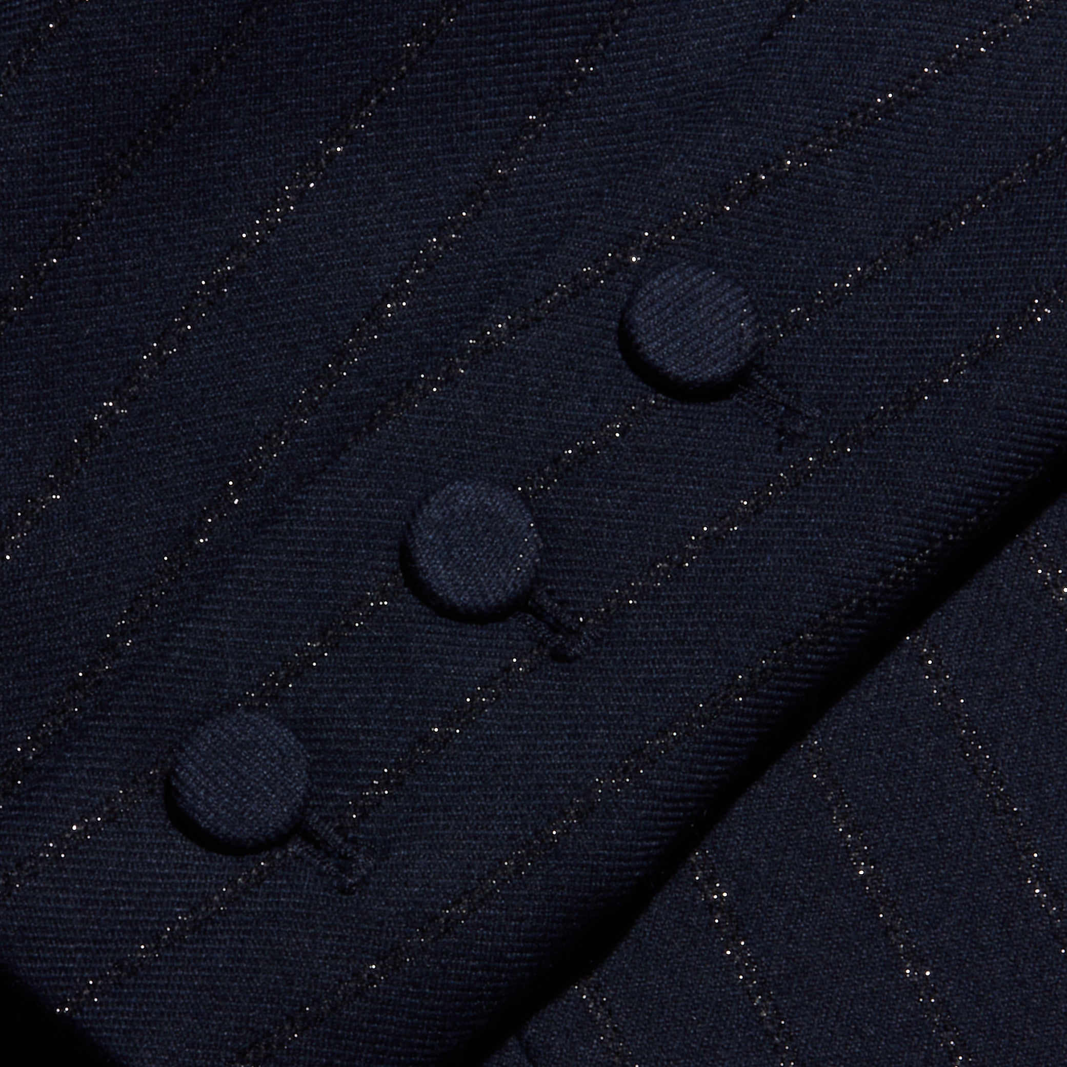 Close-up of the Risa Double-Breasted Blazer sleeve featuring three fabric-covered buttons in a row, highlighting the fine texture and subtle shimmer of Lurex woven into its dark pinstripe material.
