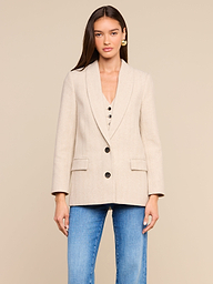 Channeling New York Fashion Week style, this woman wears the Amelie Blazer—a fitted beige blazer with black buttons—over a matching top, paired with blue jeans as she stands against a plain, light-colored background.