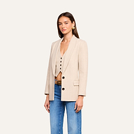 Sure Here’s a revised version incorporating the product name: A woman wears the Amelie Blazer—a beige fitted style—over a coordinating vest and blue jeans, standing against a plain background. With long straight hair, gold earrings, and a neutral expression, she exudes an effortless look reminiscent of New York Fashion Week.