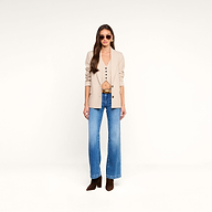 A woman with long hair wearing sunglasses, the Amelie Blazer in beige over a matching vest, blue jeans, and brown boots stands against a plain white background.
