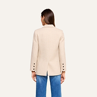 A woman with straight brown hair is shown from the back wearing the fitted Amelie Blazer in beige, featuring button details on the sleeves, paired with blue jeans against a plain light background.