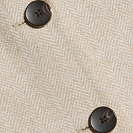 Close-up of cream-colored herringbone tweed fabric with two dark, round, four-hole buttons sewn onto it. The texture and weave of the fabric are clearly visible, embodying the tailored elegance of the Amelie Blazer—a fitted piece inspired by New York Fashion Week.