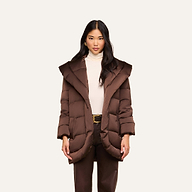 A woman wearing the Glacier Shawl Puffer Jacket—a brown water-repellent puffer with a wide collar—paired with a cream turtleneck and brown pants, stands against a plain light background.