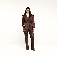 A woman stands against a white background wearing the Glacier Shawl Puffer Jacket, styled with wide-legged brown pants, brown shoes, and a beige turtleneck sweater.