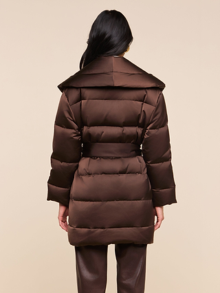 A person with long dark hair, seen from behind, wears the Glacier Shawl Puffer Jacket—a brown water-repellent puffer with a wide collar—paired with matching brown pants against a plain beige background.