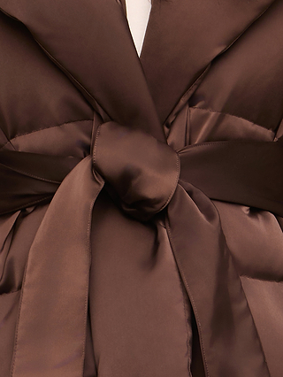 Close-up of the Glacier Shawl Puffer Jacket in brown satin, featuring a wide collar and a matching belt tied in a knot at the waist, showcasing the elegant drape reminiscent of a classic shawl jacket.