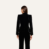A woman stands with her back to the camera, wearing the fitted Philippa Velvet Blazer with satin lapels and matching black pants against a plain light background.