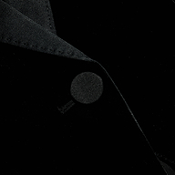 A close-up of the Philippa Velvet Blazer showcases the collar and a button, emphasizing the rich texture and folds of its black velvet fabric, while satin lapels add an elegant touch.