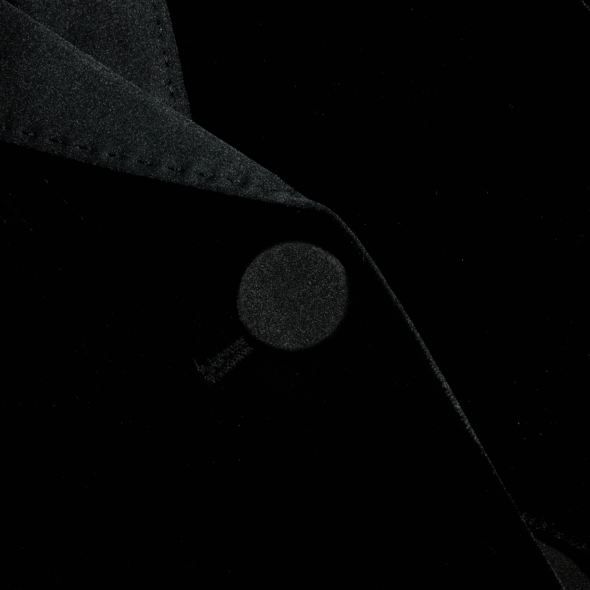 A close-up of the Philippa Velvet Blazer showcases the collar and a button, emphasizing the rich texture and folds of its black velvet fabric, while satin lapels add an elegant touch.