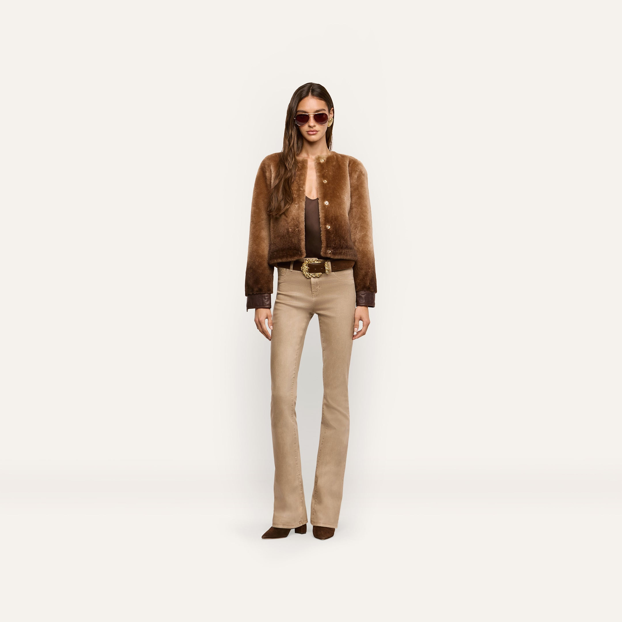 A person wearing a brown cropped Voltaire Shearling Jacket with dark cuffs, a brown top, and beige flared jeans.