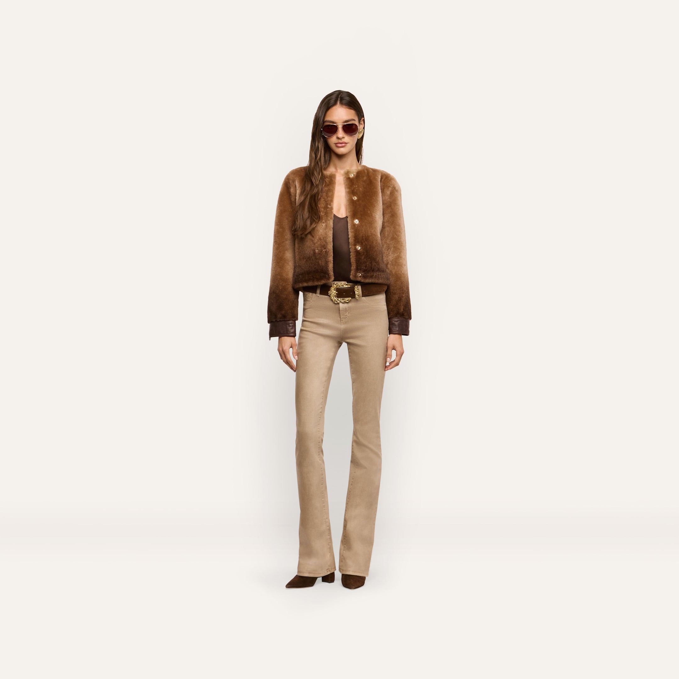 A person wearing a brown cropped Voltaire Shearling Jacket with dark cuffs, a brown top, and beige flared jeans.