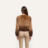 A person seen from behind wears a brown, collarless cropped Voltaire Shearling Jacket with dark brown cuffs.