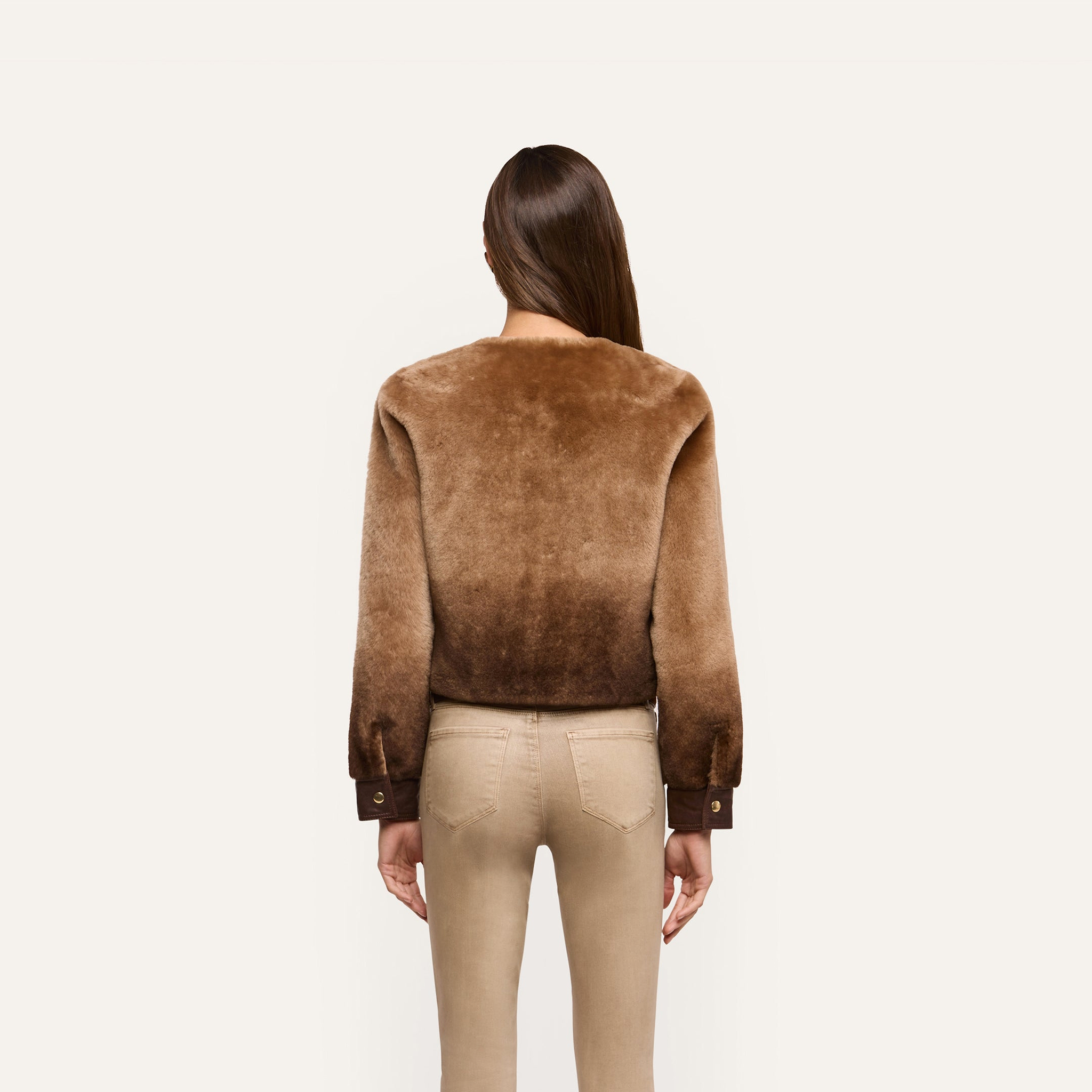 A person seen from behind wears a brown, collarless cropped Voltaire Shearling Jacket with dark brown cuffs.