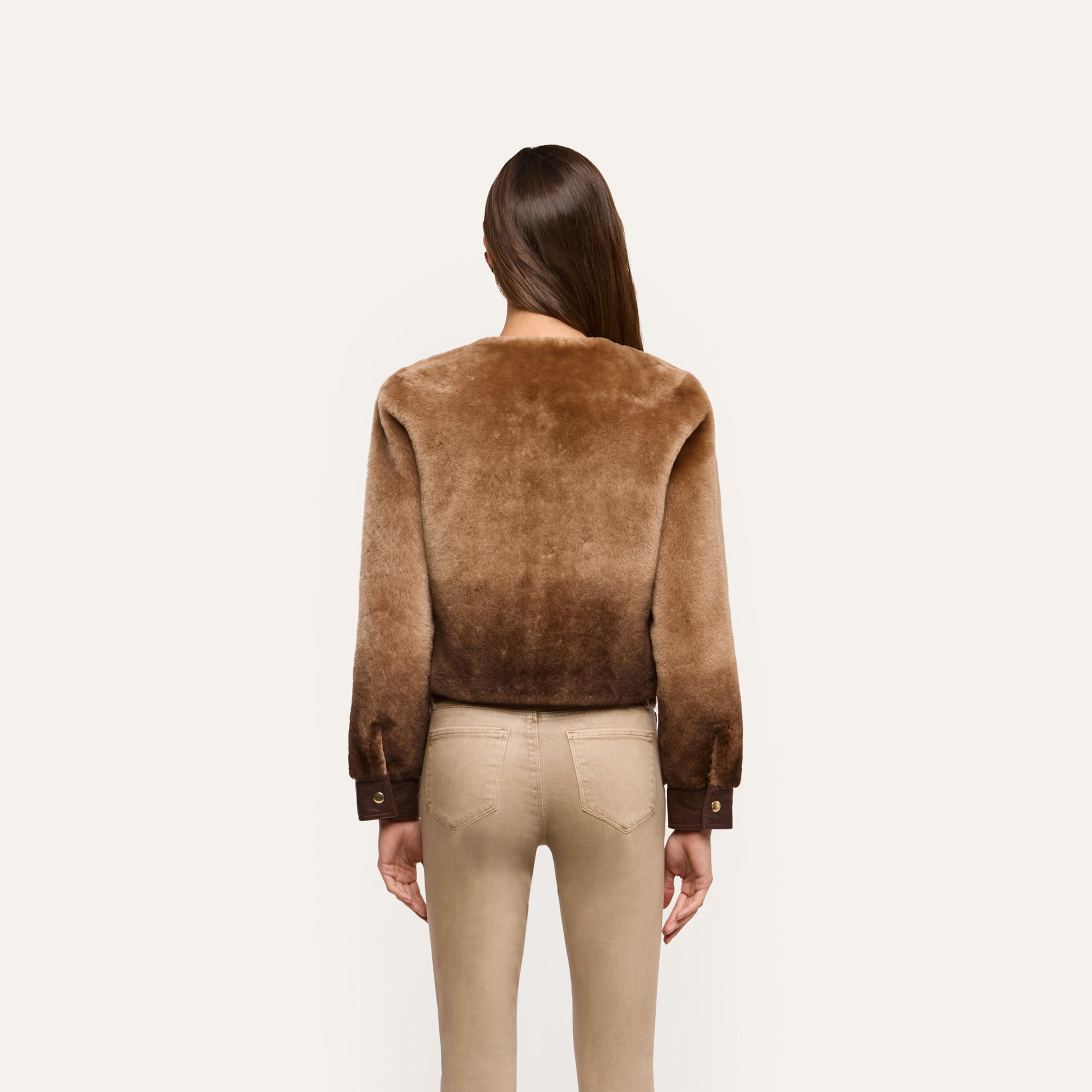 A person seen from behind wears a brown, collarless cropped Voltaire Shearling Jacket with dark brown cuffs.