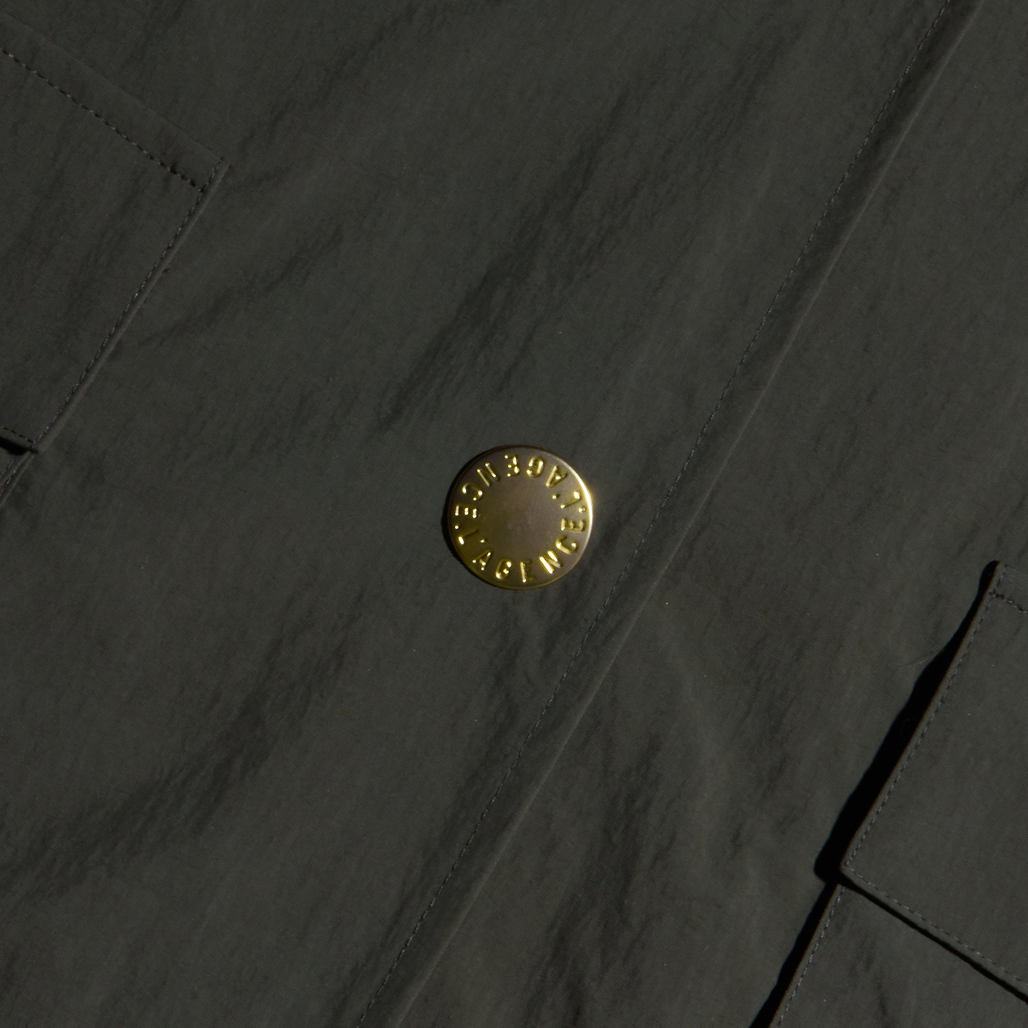 Close-up of the Axel Windbreaker Trench, a dark fabric utility jacket featuring large, round gold buttons engraved with “Burberry London England” and two rectangular front pockets.