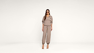 A woman wearing sunglasses, a taupe zip-up top, and matching jogger pants stands against a plain white background, looking straight ahead.