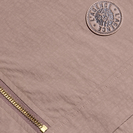 Close-up of the Vex Cropped Windbreaker, a mauve activewear jacket featuring a gold zipper and a round embroidered patch with a lion’s head and the word LAGENCE repeated twice around the border.