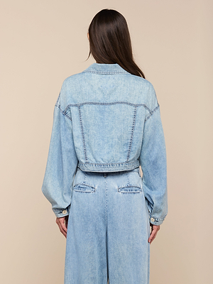 A person with long brown hair, seen from behind, wears the Gaines Jean Jacket with balloon sleeves and matching high-waisted jeans in featherweight denim against a plain beige background.