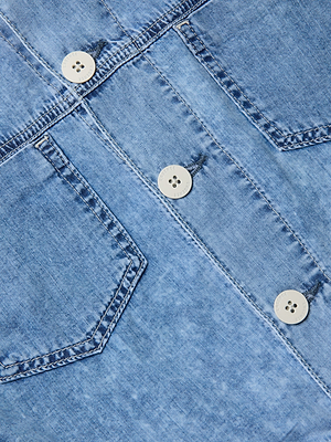 Close-up of the Gaines Jean Jacket in light blue denim, featuring two chest pockets with pointed flaps, three white buttons along the center seam, visible stitching, and a slightly faded texture.
