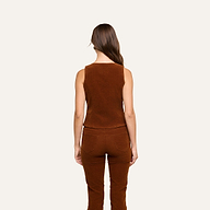 A woman with long brown hair, wearing the Yelena Vest and casual corduroy pants, stands facing away against a plain light background.